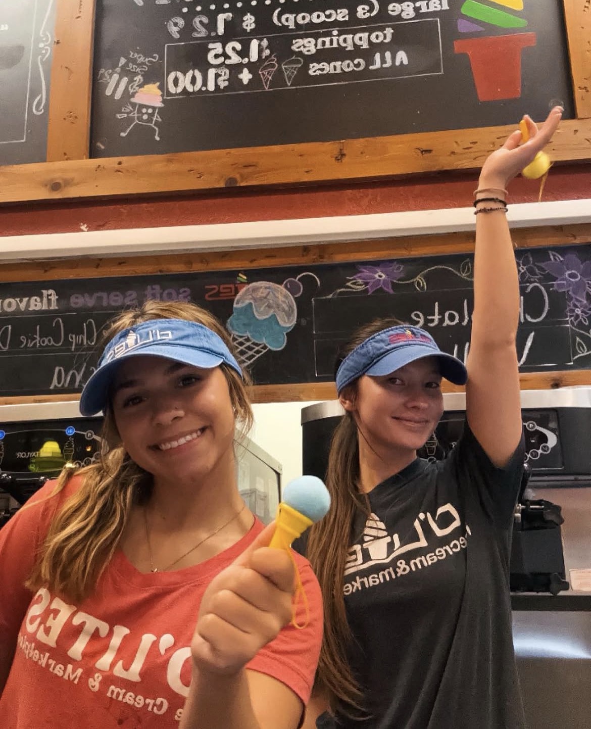 Two D'Lites staff members smiling in uniform and visors inside the shop